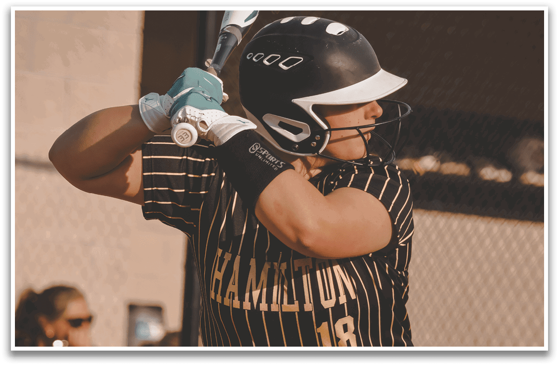 A woman wearing a black and gold baseball uniform is swinging a bat. Description generated by AI