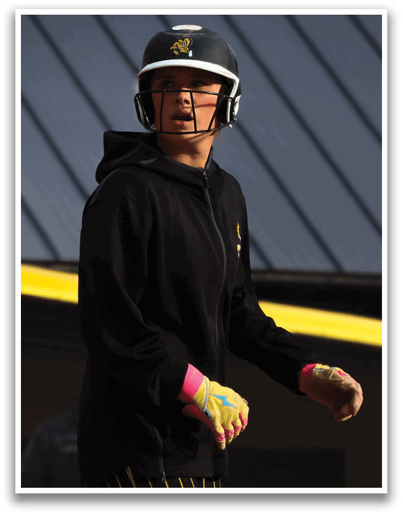 A woman wearing a black helmet and a black and yellow shirt is standing on a baseball field. Description generated by AI
