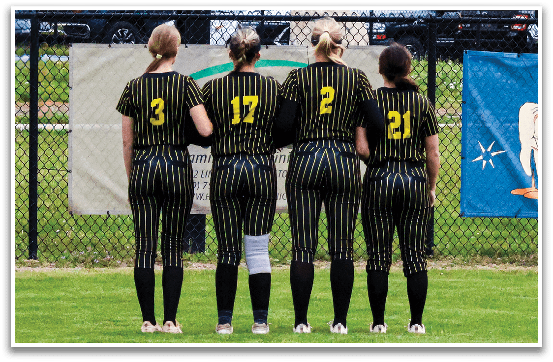 A group of four women standing in front of a scoreboard. Description generated by AI