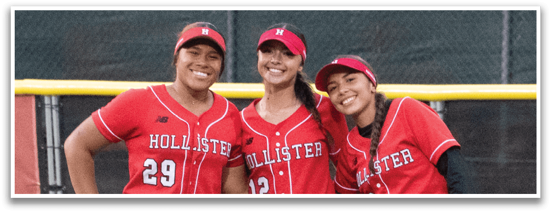 Three girls wearing red and black uniforms are standing on a grassy field. Description generated by AI