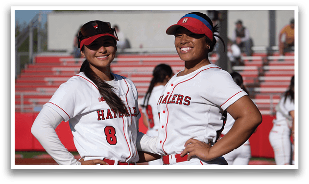 Two female baseball players wearing red and white uniforms. Description generated by AI