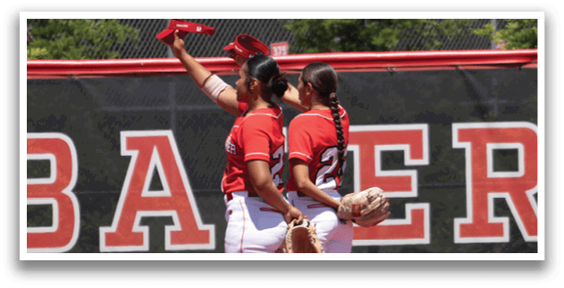 Two girls standing on a baseball field. Description generated by AI