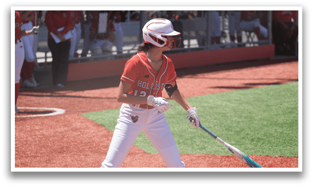 A female baseball player in a red shirt and white pants holding a bat. Description generated by AI