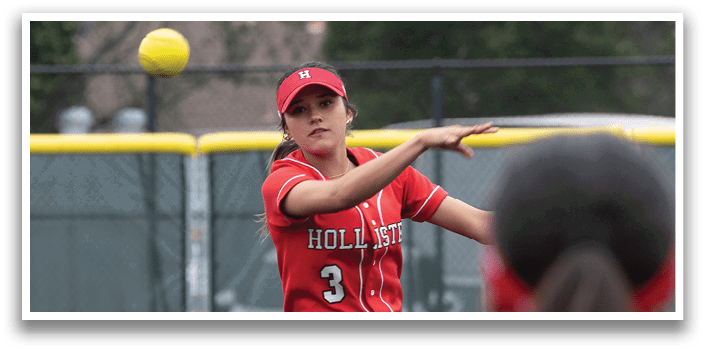 A woman in a red shirt is pitching a ball. Description generated by AI