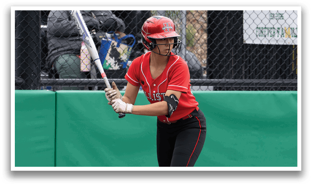 A woman in a red shirt and black shorts is holding a bat and getting ready to hit a ball. Description generated by AI