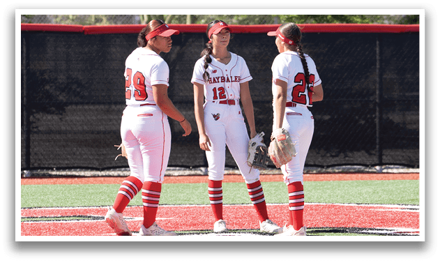 Three female softball players standing on a field. Description generated by AI