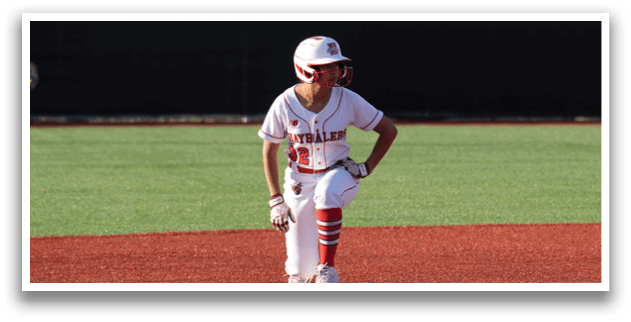 A boy in a red and white uniform is sitting on the ground on a baseball field. Description generated by AI