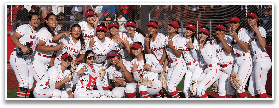 A group of girls in white and red uniforms pose for a picture on a baseball field. Description generated by AI