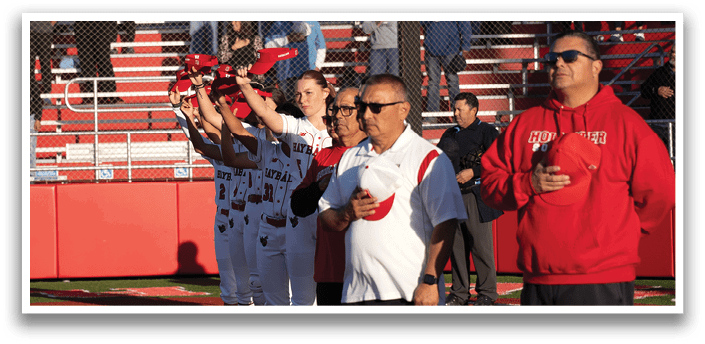A group of people stand on a baseball field, some of them wearing red and white uniforms. They are holding up their hands in the air, possibly celebrating a victory or showing support for their team. The crowd of people is gathered around the field, watching the event. AI generated content