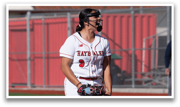 A female baseball player is standing on the pitcher's mound, wearing a red and white uniform. She is holding a baseball in her hand and appears to be preparing to throw it. There are two other people in the scene, one standing behind her and another to the right. AI generated content