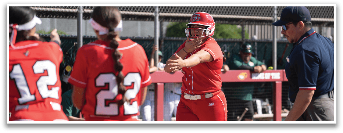 A group of women in red uniforms are playing a game of softball. One woman is pitching the ball while another woman is holding a baseball bat, ready to swing. A man in a blue shirt is watching the game and wearing a baseball glove. AI generated content