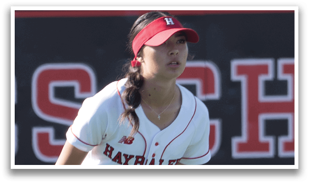 A female baseball player is standing on the field, wearing a white uniform and a red hat. She is holding a baseball glove in her hand. AI generated content