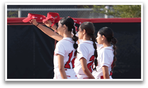 Three female softball players are standing on a field, wearing white uniforms and red socks. They are holding their gloves in the air, possibly celebrating a successful play or preparing for the next one. AI generated content