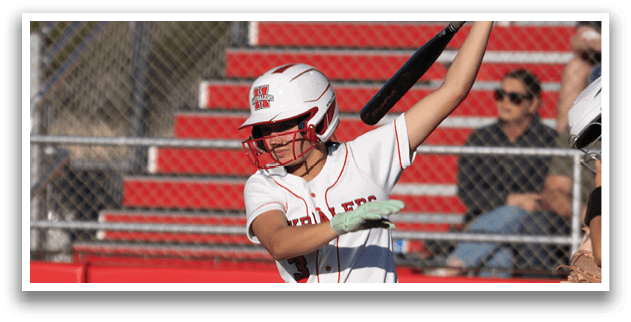 A woman in a white and red baseball uniform is swinging a bat. Description generated by AI