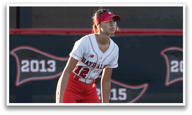 A woman wearing a red and white uniform is standing on a baseball field. Description generated by AI
