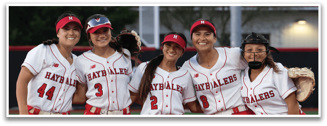 Five female softball players standing on a field. Description generated by AI