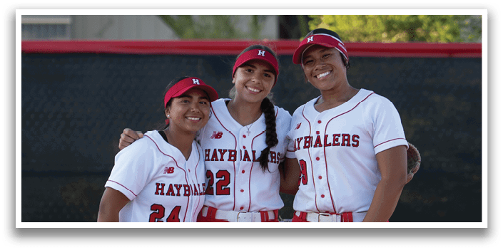 Three women standing on a baseball field. Description generated by AI