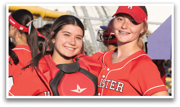 Two girls wearing red and black baseball uniforms. Description generated by AI