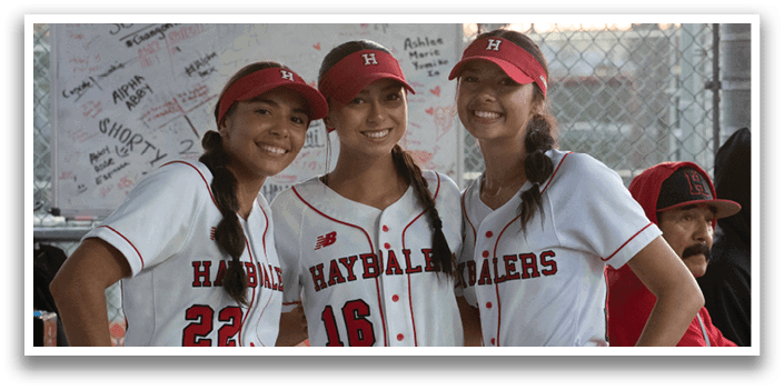 Three girls wearing baseball uniforms. Description generated by AI