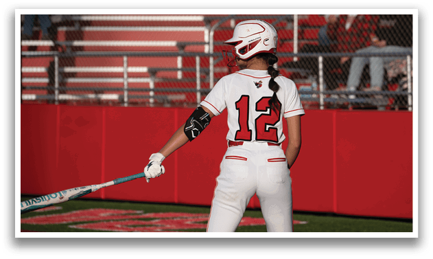 A woman wearing a white and red baseball uniform is holding a bat. Description generated by AI