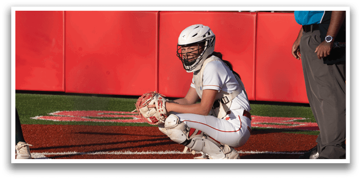 A female baseball player wearing a helmet and kneeling on the ground. Description generated by AI