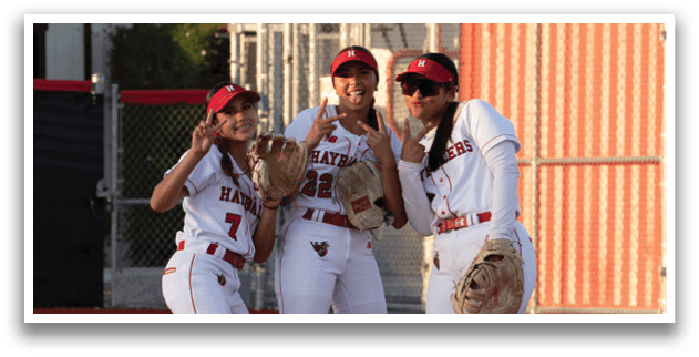 Three girls standing on a baseball field. Description generated by AI