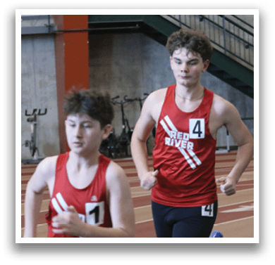 Three young men are running on a track, wearing red shirts and black shorts. They are in a race, with one of them leading the pack. AI generated content