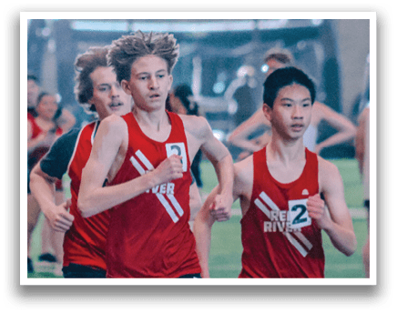 Three young men are running on a track, wearing red shirts and shorts. They are in a race, with one of them leading the pack. AI generated content