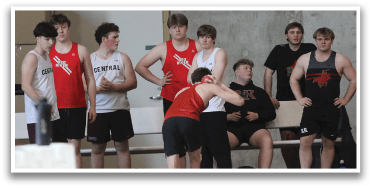 A group of young men are gathered in a gym, some standing and some sitting. They are wearing sports uniforms and are engaged in conversation. AI generated content