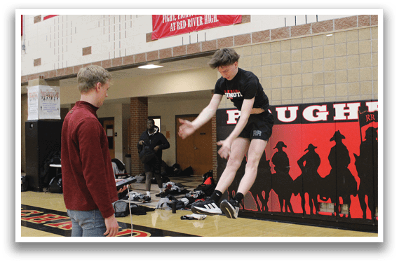 A man is jumping in the air in front of a banner that says Rough Riders. Description generated by AI