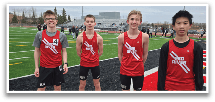 Three boys wearing red shirts and black shorts stand on a field. Description generated by AI