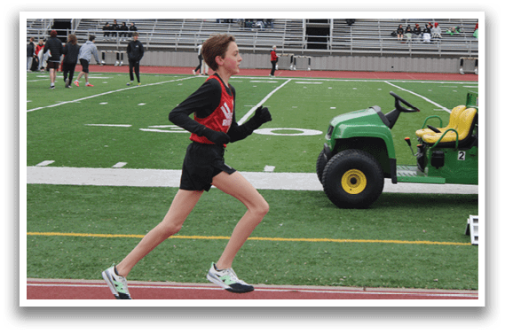 A boy running on a field with a green tractor behind him. Description generated by AI
