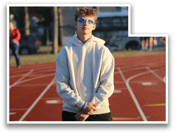 A man wearing a white hoodie and sunglasses standing on a track. Description generated by AI