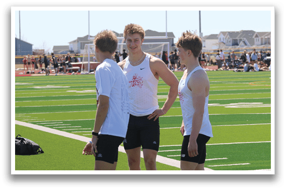 Three young men standing on a grass field. Description generated by AI