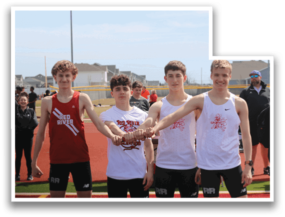 Four boys standing on a track, wearing white shirts and black shorts. Description generated by AI