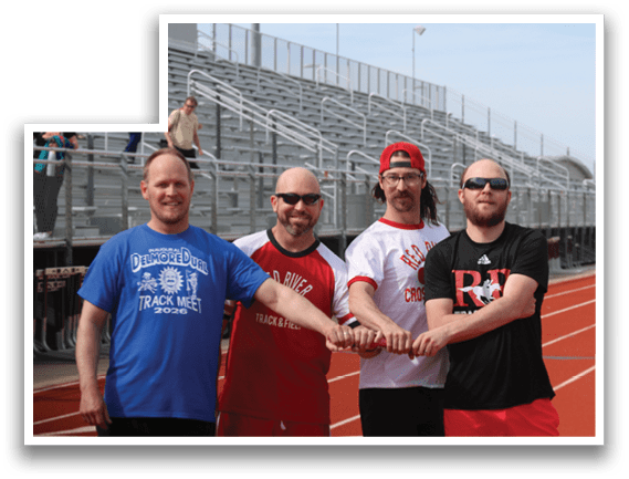 Four men wearing red and white shirts and red shorts pose for a picture on a track. Description generated by AI