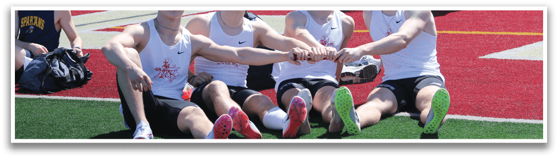 Four young men sitting on a field. Description generated by AI