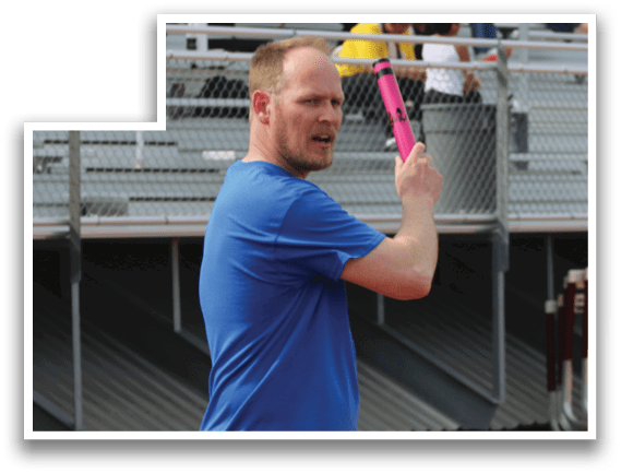 A man holding a pink bat on a track. Description generated by AI