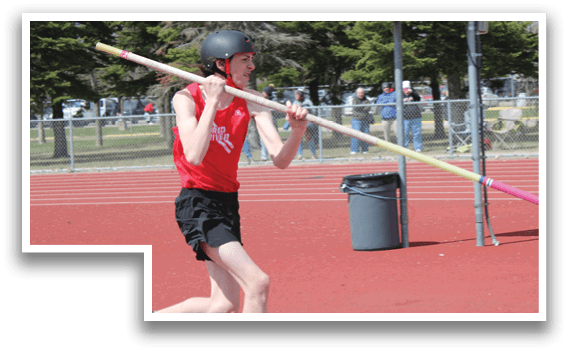A man in a red shirt and black shorts is running on a track while holding a pole. Description generated by AI