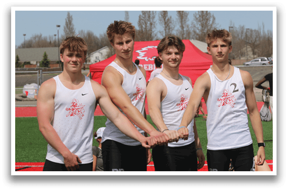 Four men wearing black shorts and white shirts pose for a picture. Description generated by AI