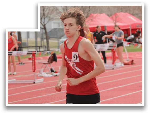 A man running on a track with a red shirt and black shorts. Description generated by AI