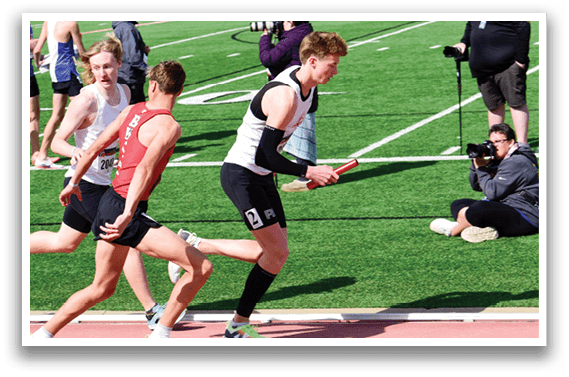 A man running on a track with a camera man behind him. Description generated by AI