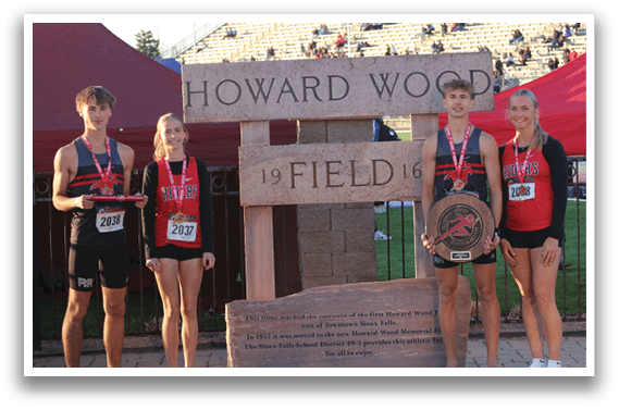 A group of people standing in front of a sign that says Howard Wood Field. Description generated by AI