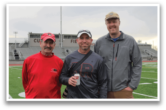 Three men standing on a football field. Description generated by AI
