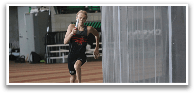 A man running on a track with a green wall behind him. Description generated by AI