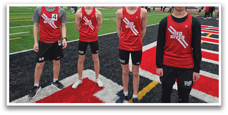 Three boys wearing red shirts and black shorts stand on a field. Description generated by AI