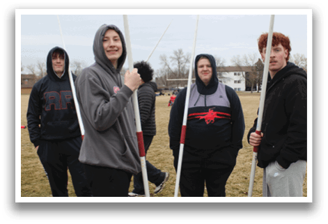 Four people standing in a field holding white poles. Description generated by AI