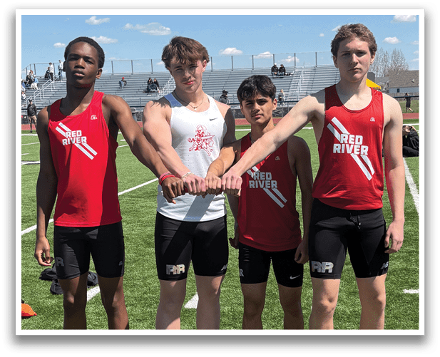 Five men wearing red and white shirts and black shorts are standing on a grass field. Description generated by AI