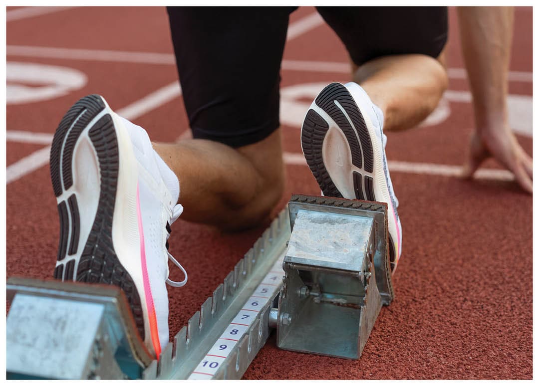 A runner is on a track, wearing a pair of shoes and leaning over a metal device. Contenido generado con IA