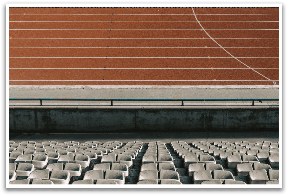 A stadium with a track and field is shown. The seats are empty, and there is a bench in the foreground. Contenido generado con IA